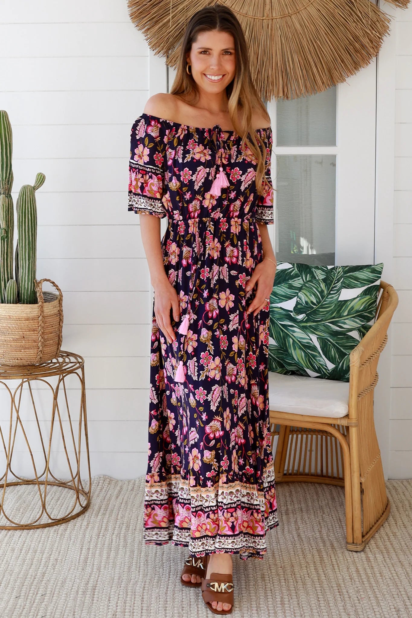 Woman in a floral dress standing under a straw umbrella in a tropical setting.