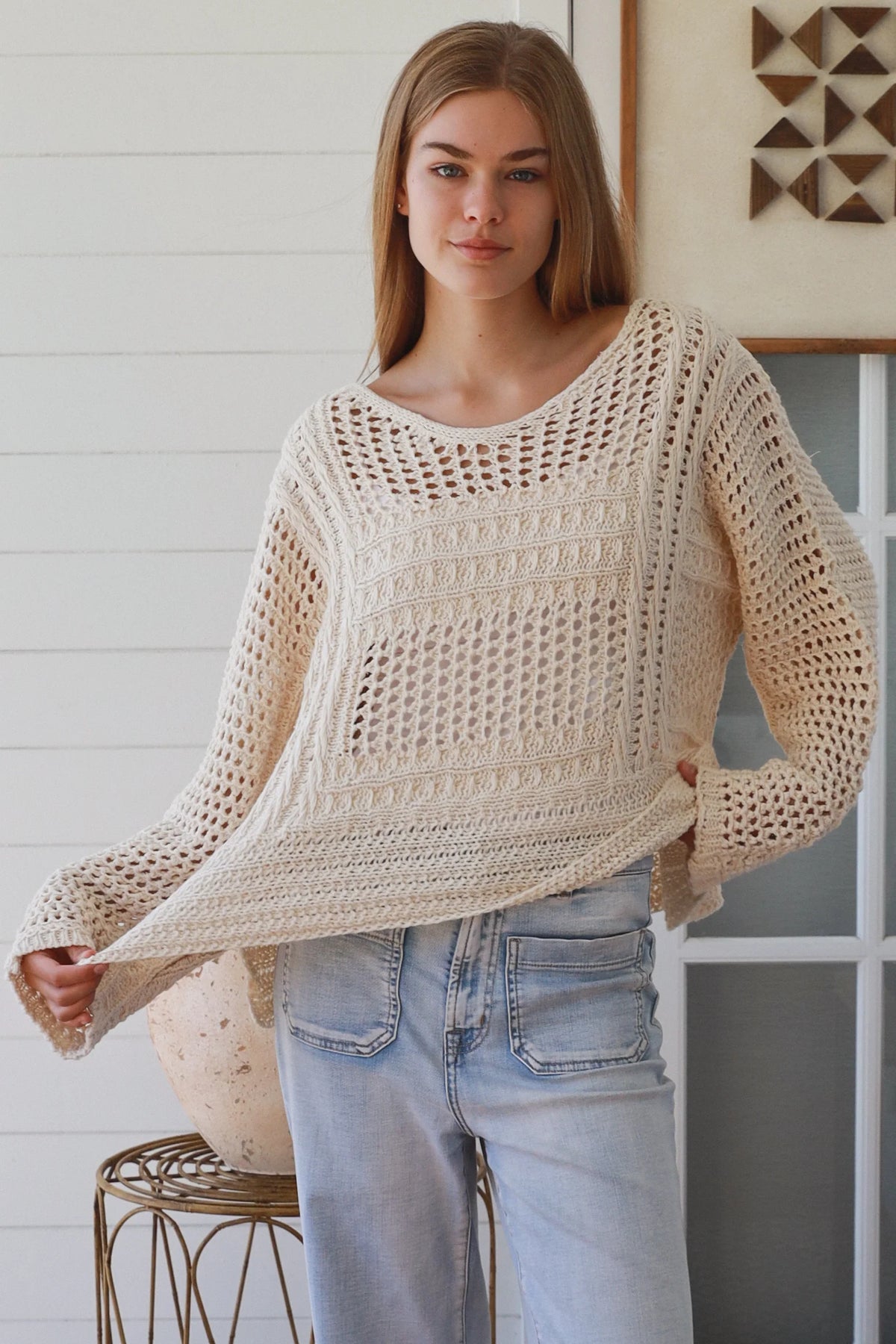 Woman wearing a beige crochet sweater and blue jeans indoors.
