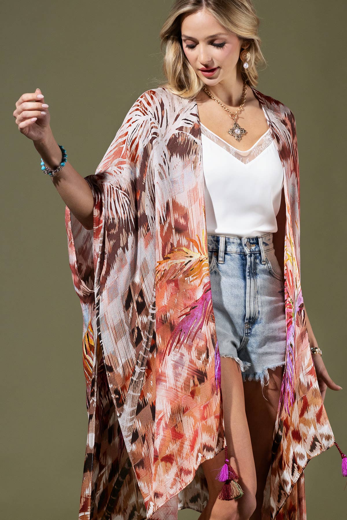 Woman wearing a colorful kimono over a white top and denim shorts on a plain background