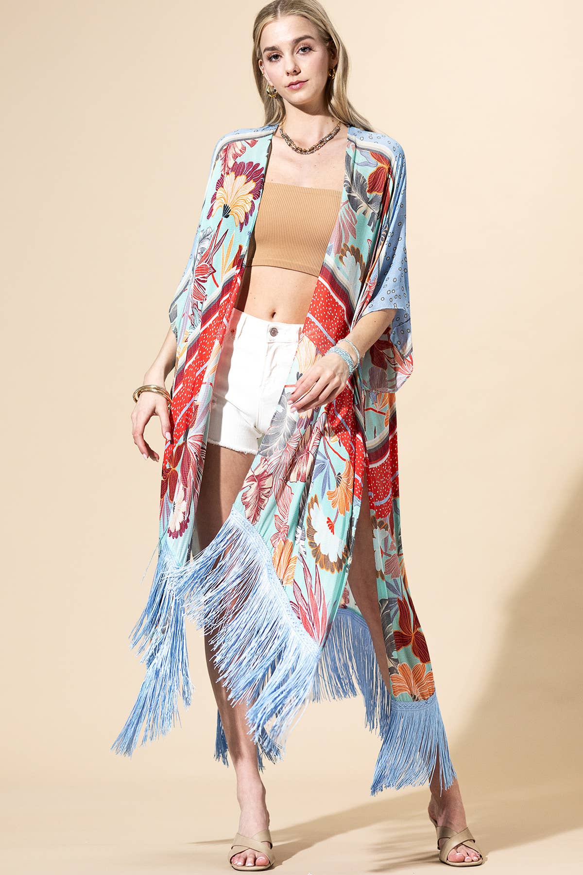 Woman wearing a colorful kimono-style cover-up with fringes on a beige background