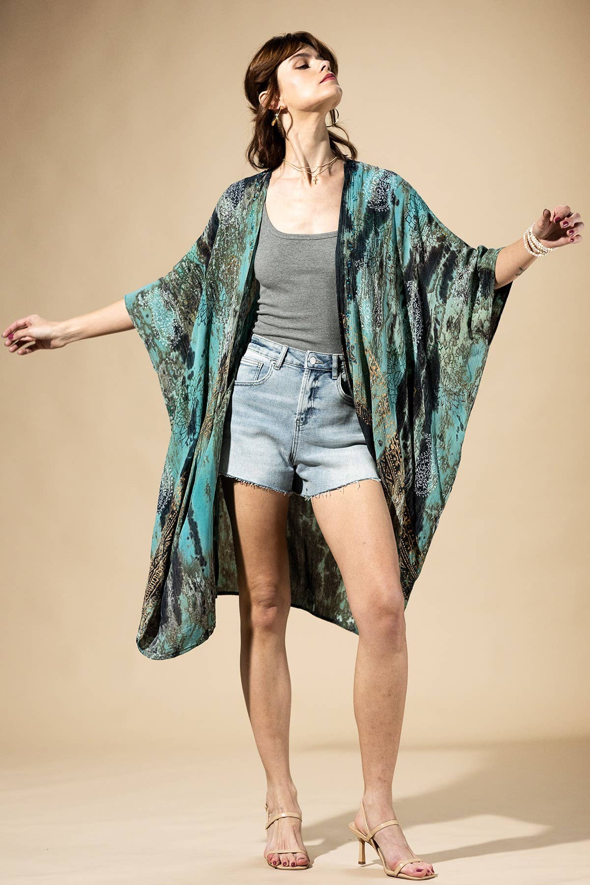 Woman wearing a long, patterned kimono over a casual outfit on a beige background