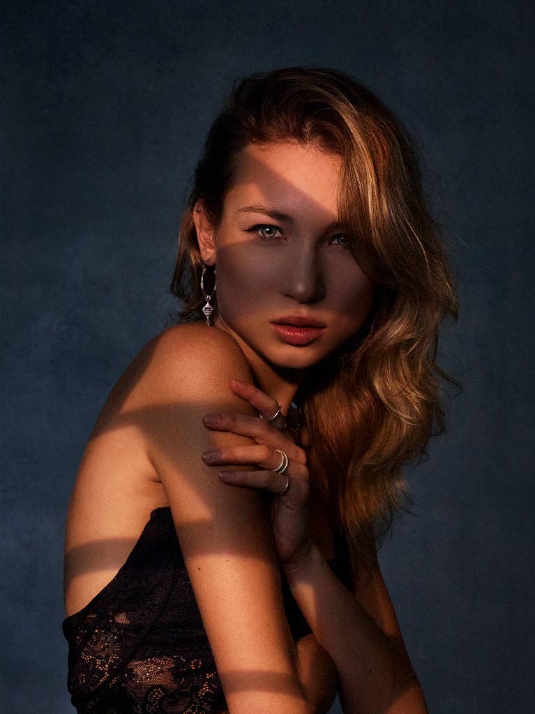 Woman posing with one arm over her shoulder against a dark background