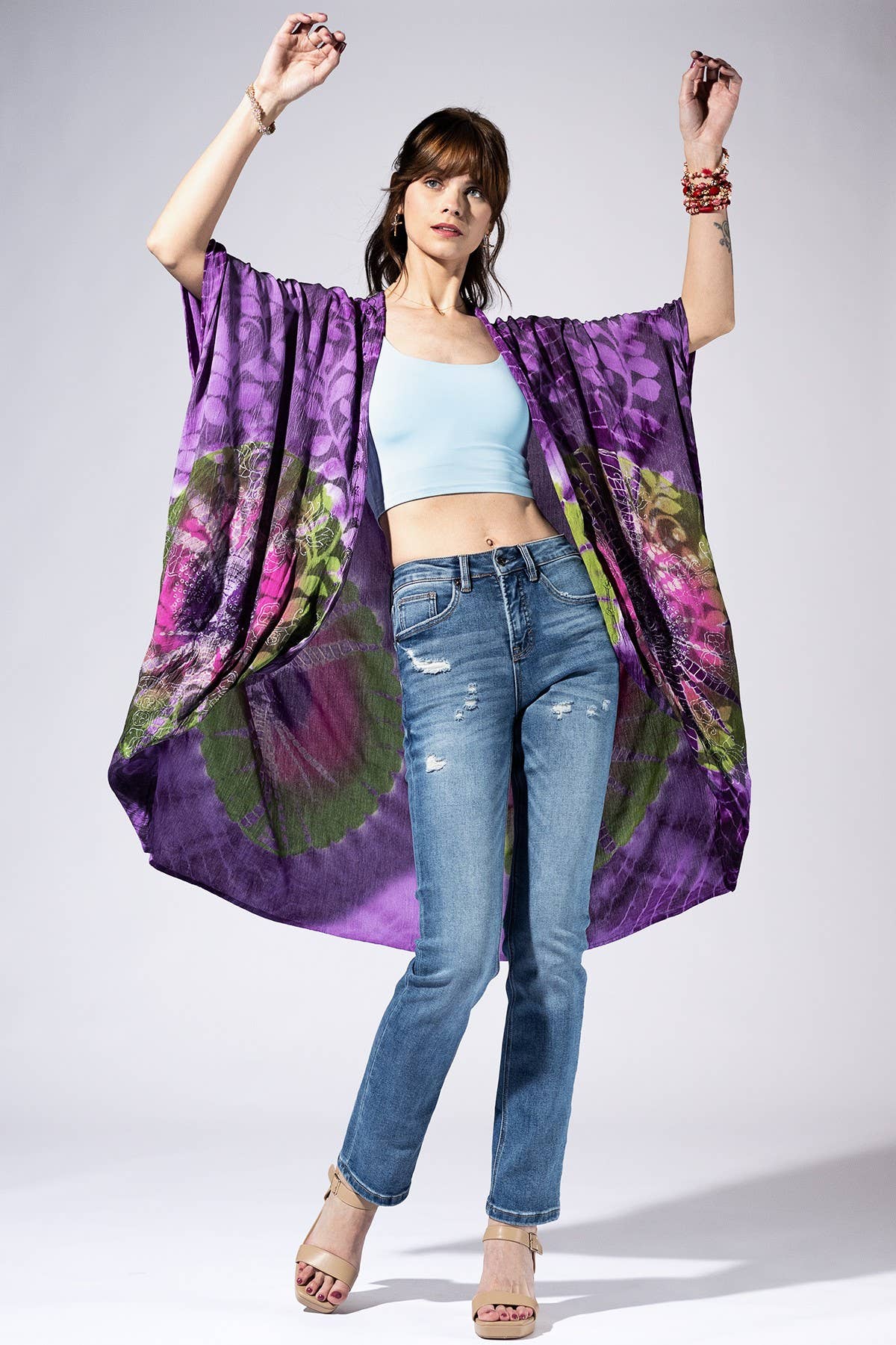 Woman wearing a colorful kimono-style garment over casual clothing on a plain background