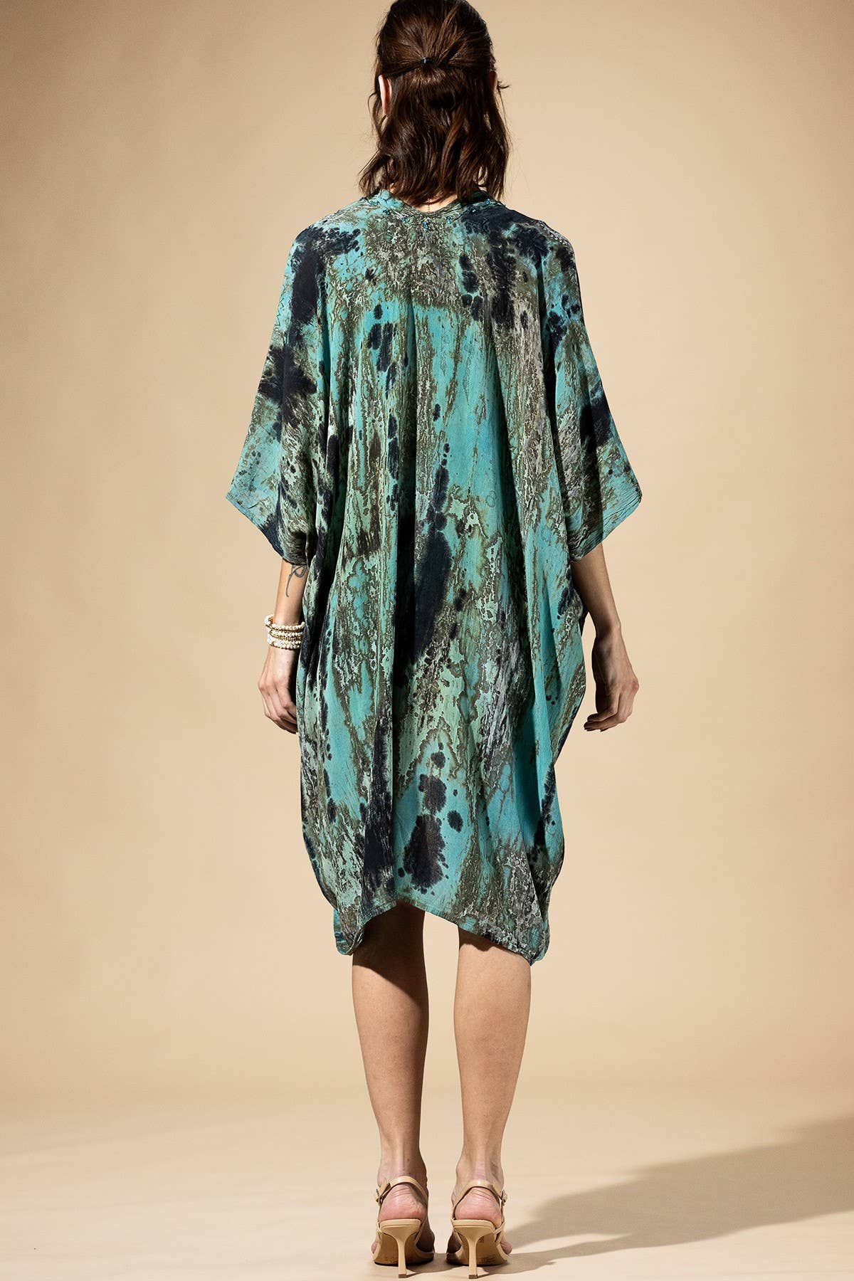Woman wearing a teal and black patterned dress against a beige background
