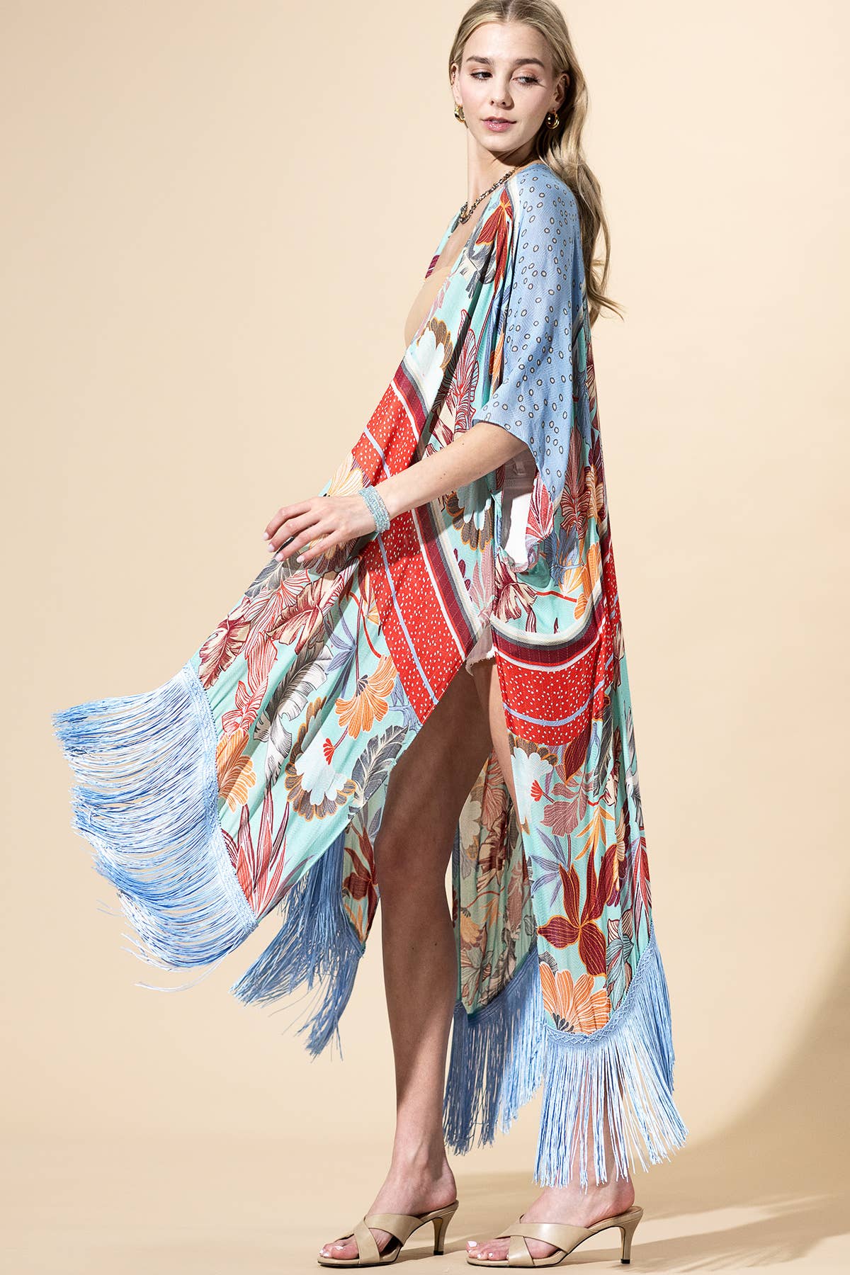 Woman wearing a colorful kimono-style dress with fringes on a beige background