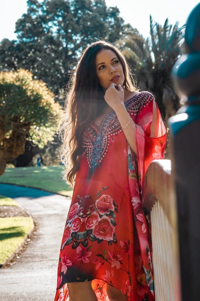 Woman in a red floral dress standing outdoors with trees in the background