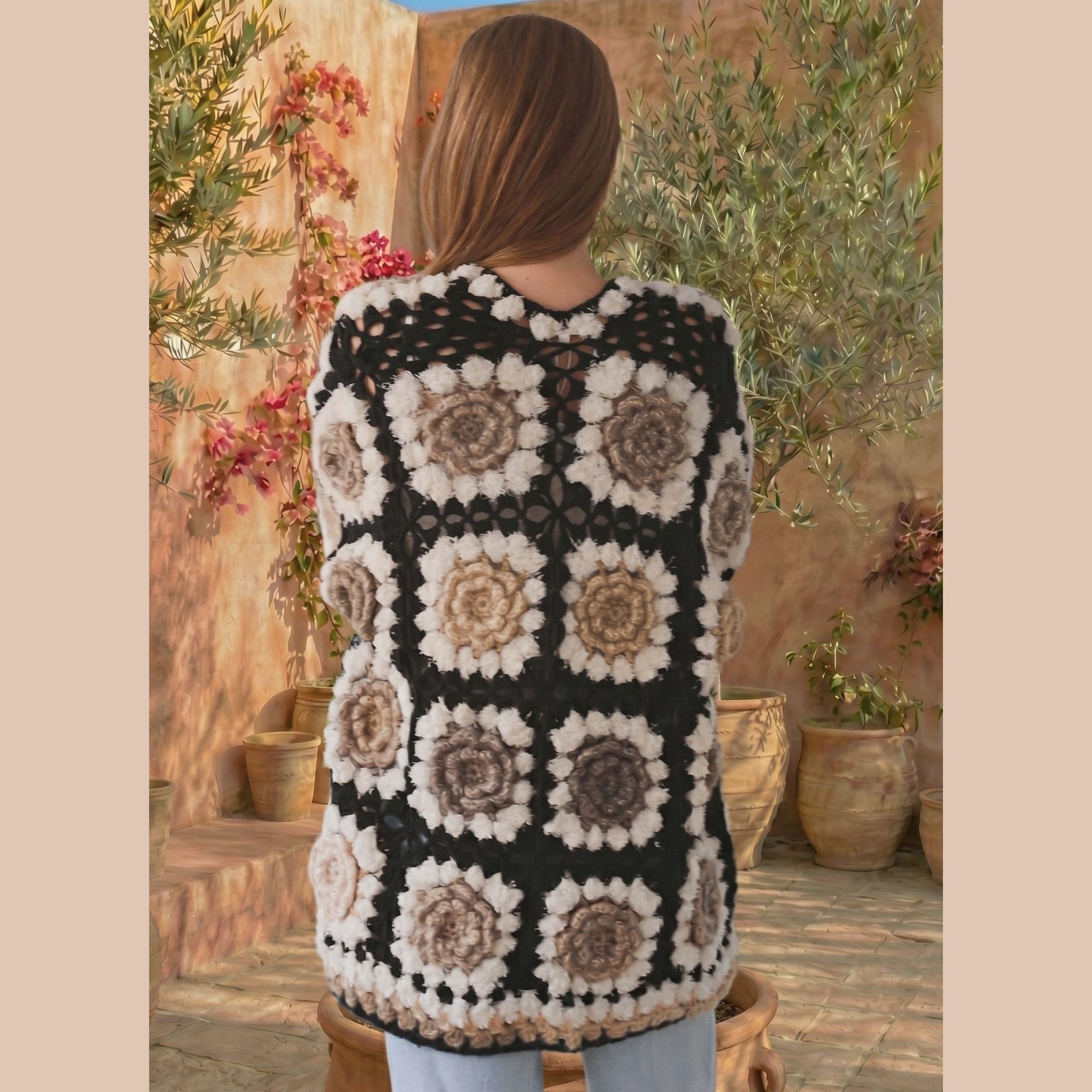 Person wearing a patterned crochet cardigan in an outdoor setting with plants and pots.