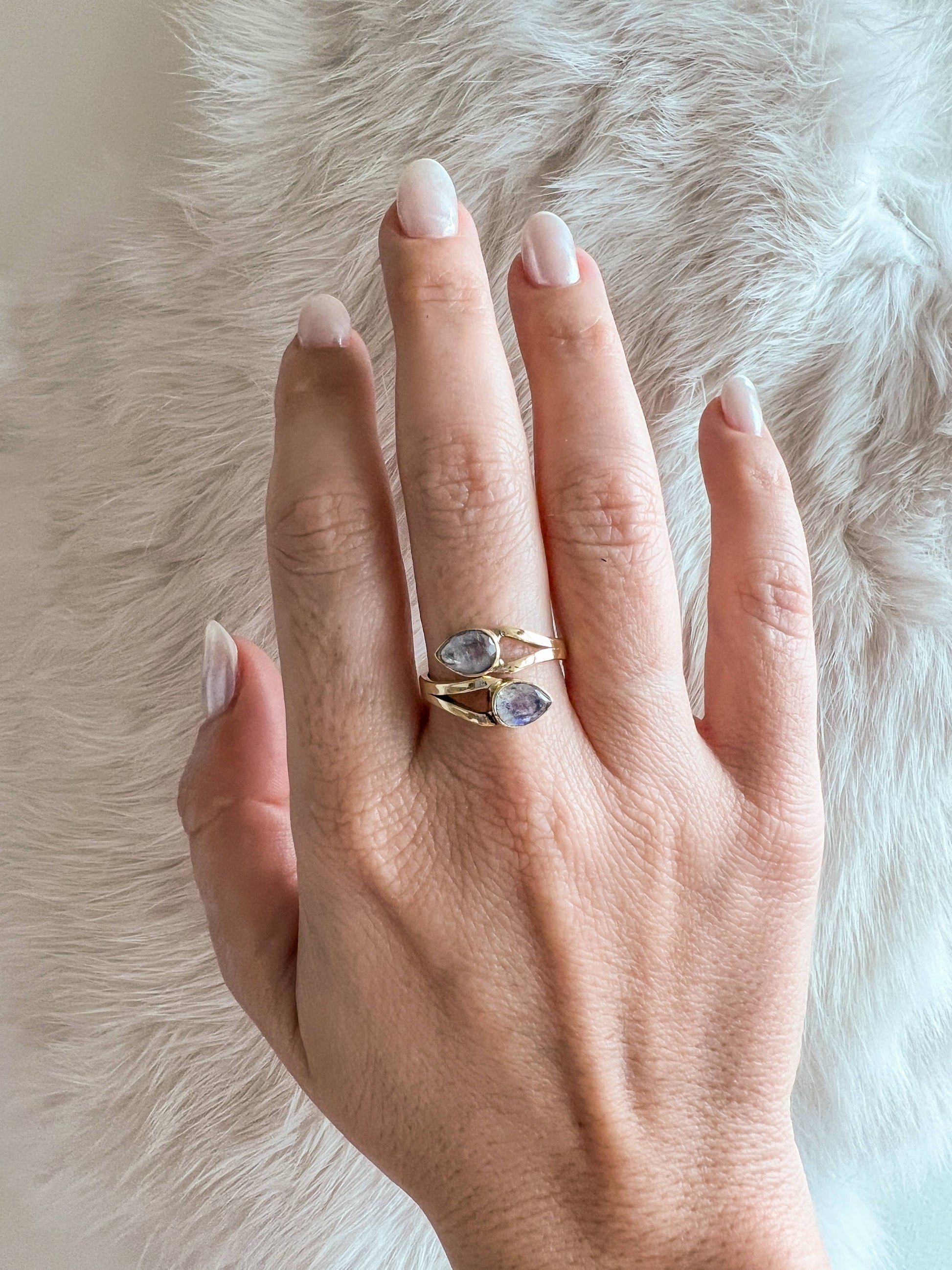 Hand wearing a gold ring with two stones on a fur background