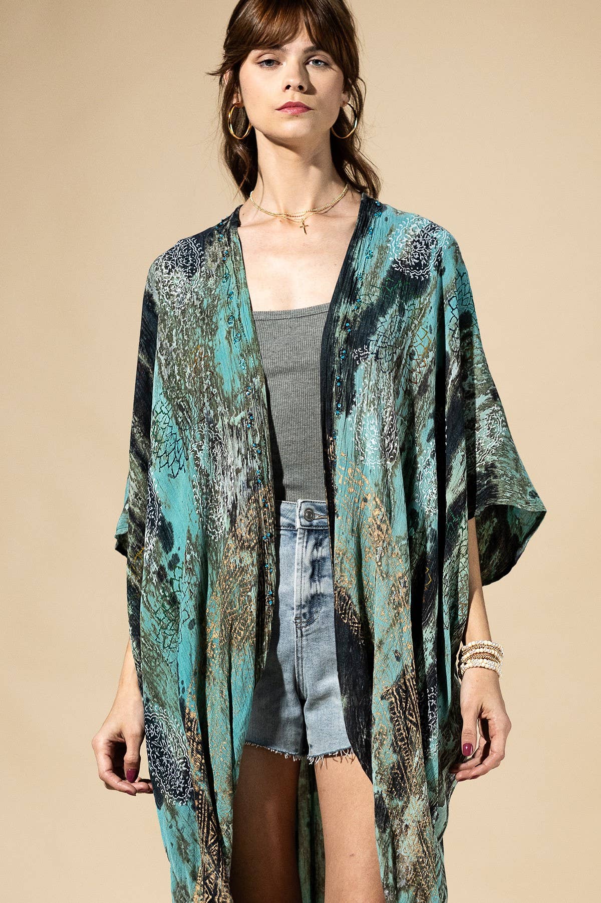 Woman wearing a patterned kimono over a gray top and denim shorts on a beige background