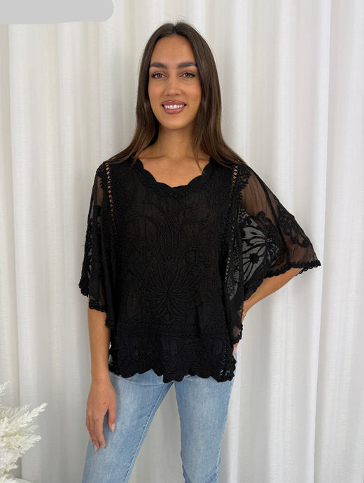 Woman wearing a black lace top and light blue jeans against a white curtain background