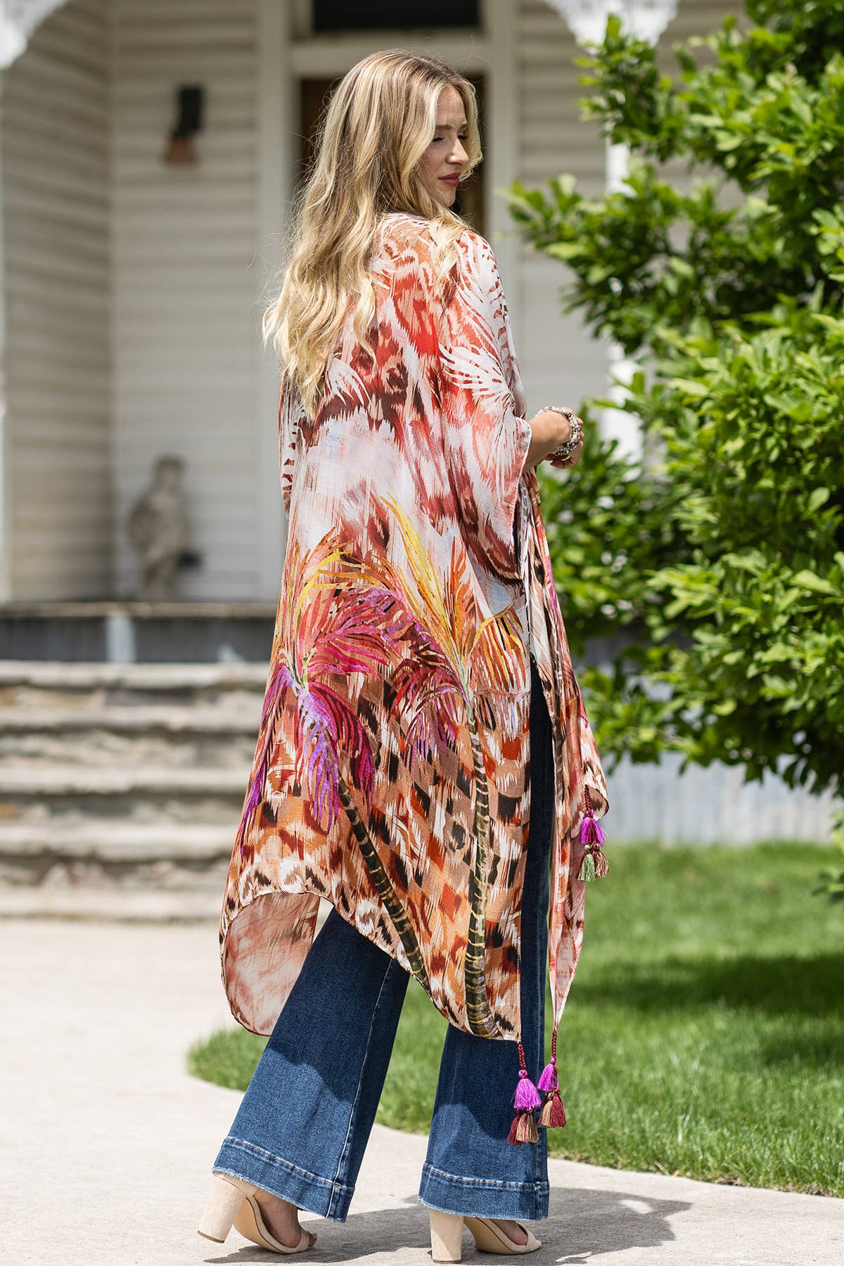 Woman wearing a colorful floral kimono in front of a house with greenery.