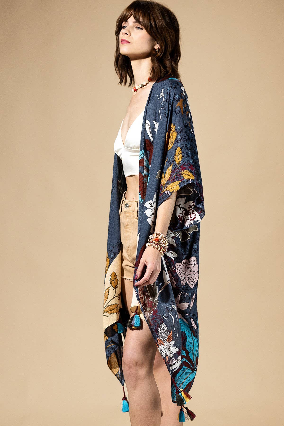 Woman wearing a floral kimono over a white top and beige pants on a beige background