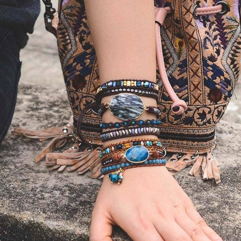 Close-up of a hand wearing multiple bracelets with a patterned bag in the background