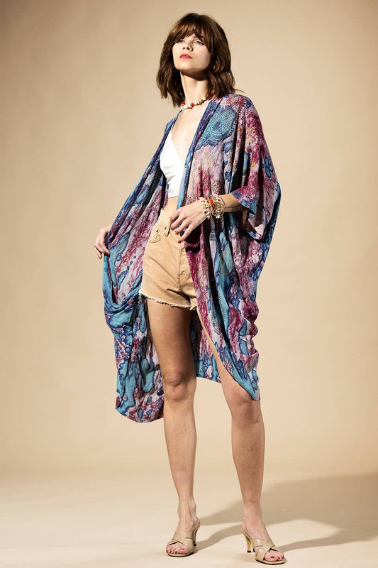 Woman wearing a colorful kimono over a white top and beige shorts on a beige background