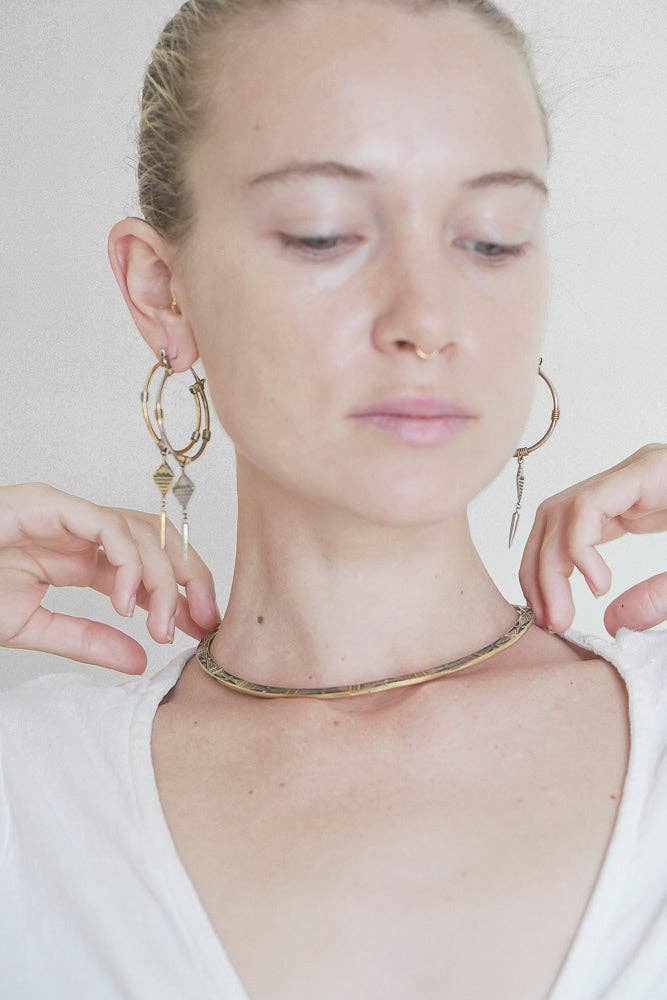 Woman wearing gold hoop earrings and a gold necklace against a plain background