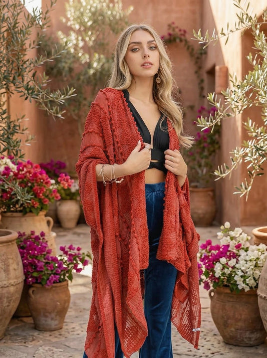Woman wearing a red cardigan over a black top and blue pants in a garden setting with flowers and pots.