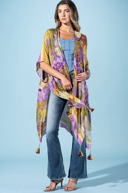 Woman wearing a colorful kimono-style garment over a blue top and jeans on a light blue background