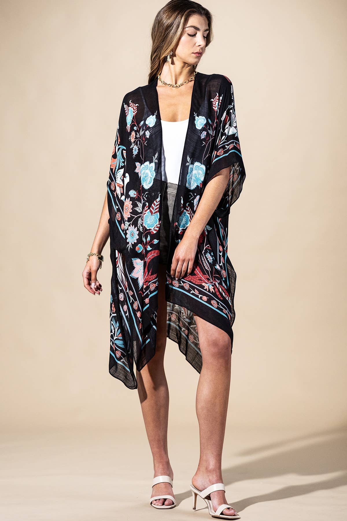Woman wearing a floral kimono over a white top and black skirt on a beige background