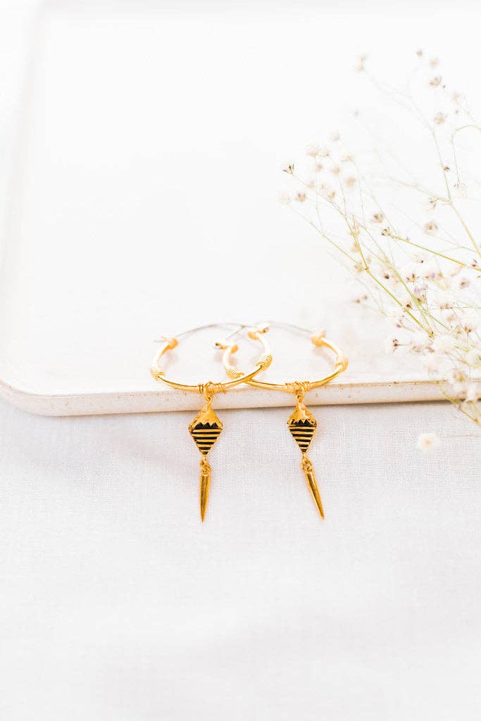 Gold earrings with black accents on a white surface with dried flowers.