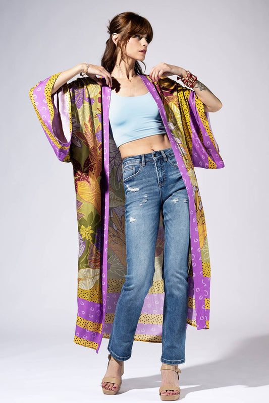 Woman wearing a colorful kimono-style garment over a light blue top and jeans on a white background