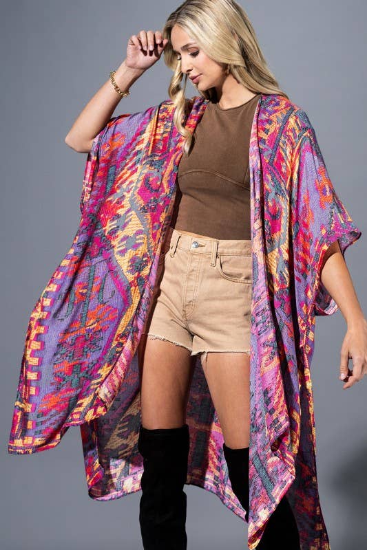 Woman wearing a colorful kimono over a brown top and beige shorts on a gray background