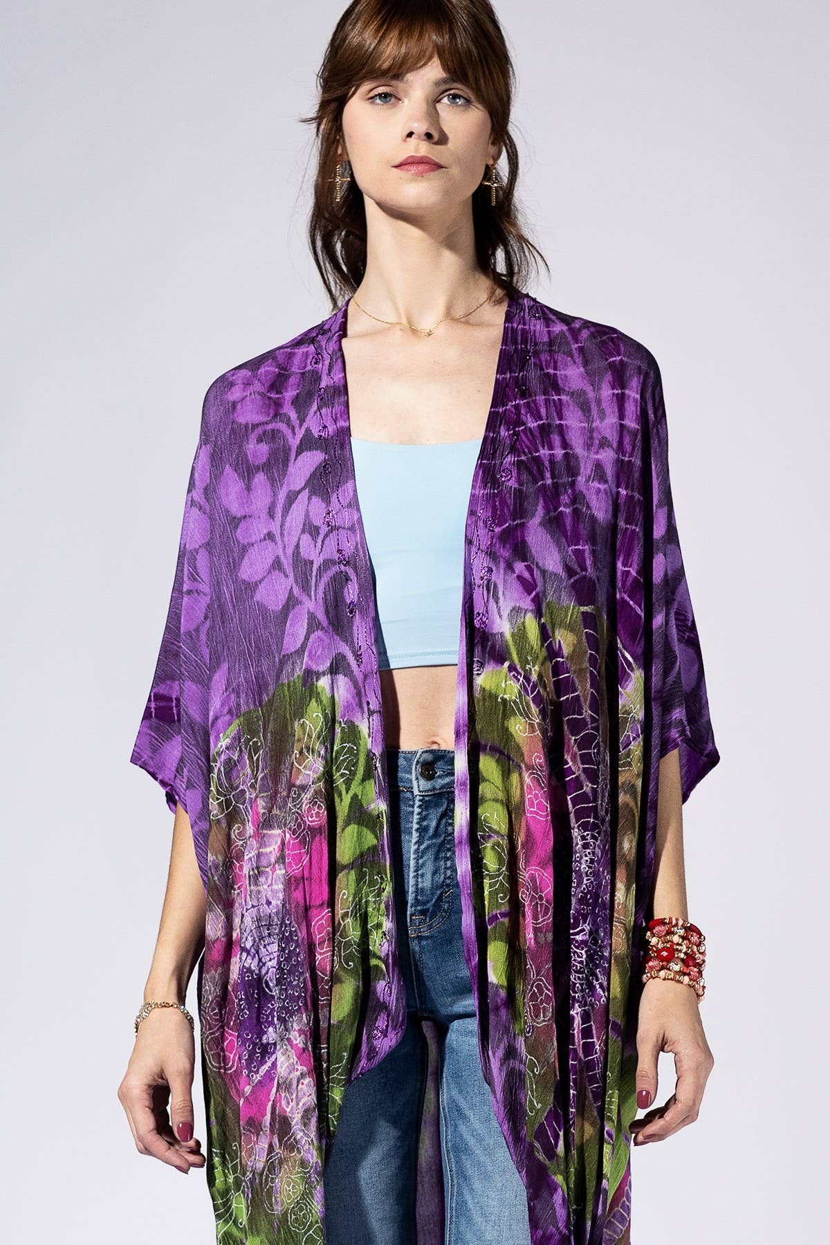 Woman wearing a purple floral kimono over a light blue top and jeans on a white background