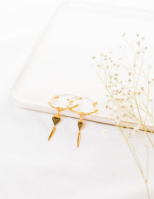 Gold spiral earrings on a white surface with dried flowers