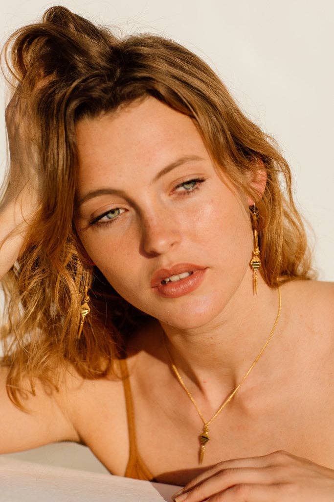 Woman with blonde hair and gold jewelry against a plain background
