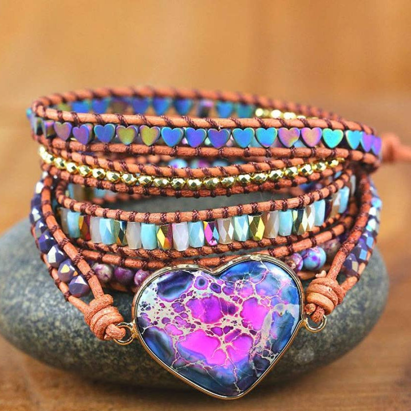 Stack of colorful beaded bracelets with a heart-shaped focal bead on a stone surface.
