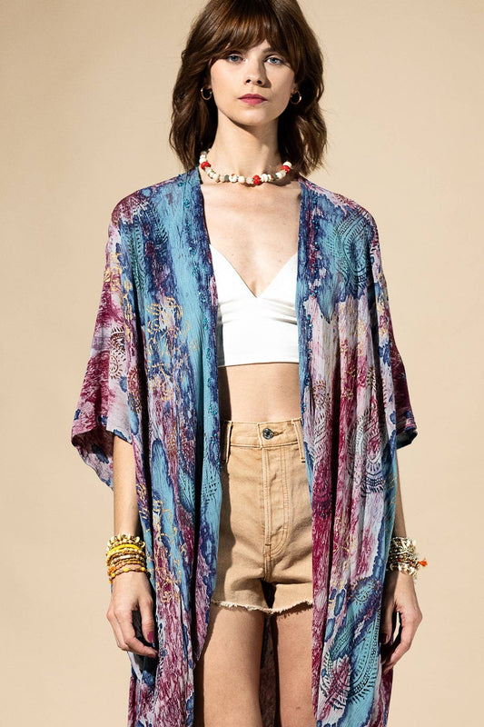 Woman wearing a colorful kimono over a white top and beige shorts on a beige background