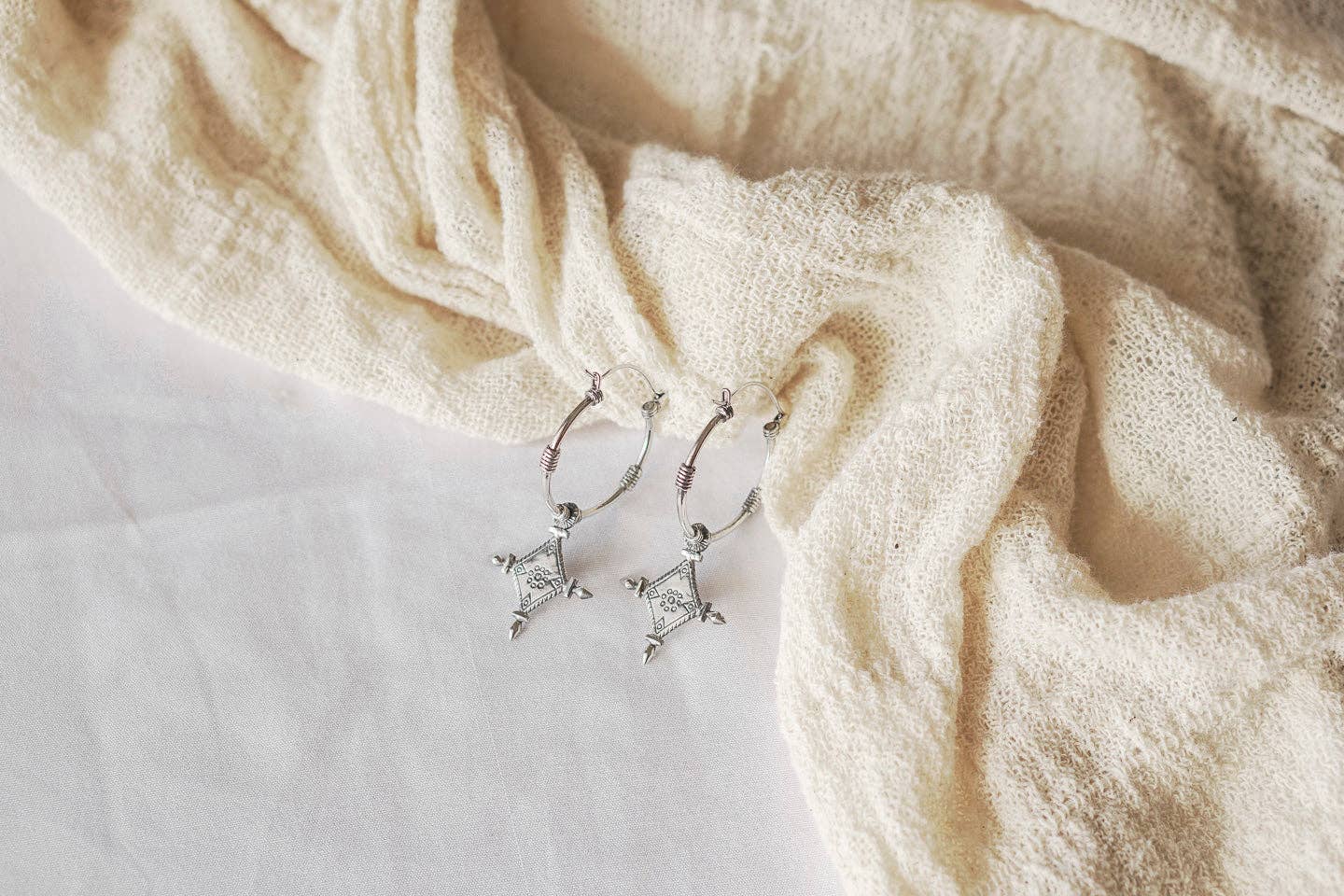 Silver hoop earrings on a textured beige fabric background