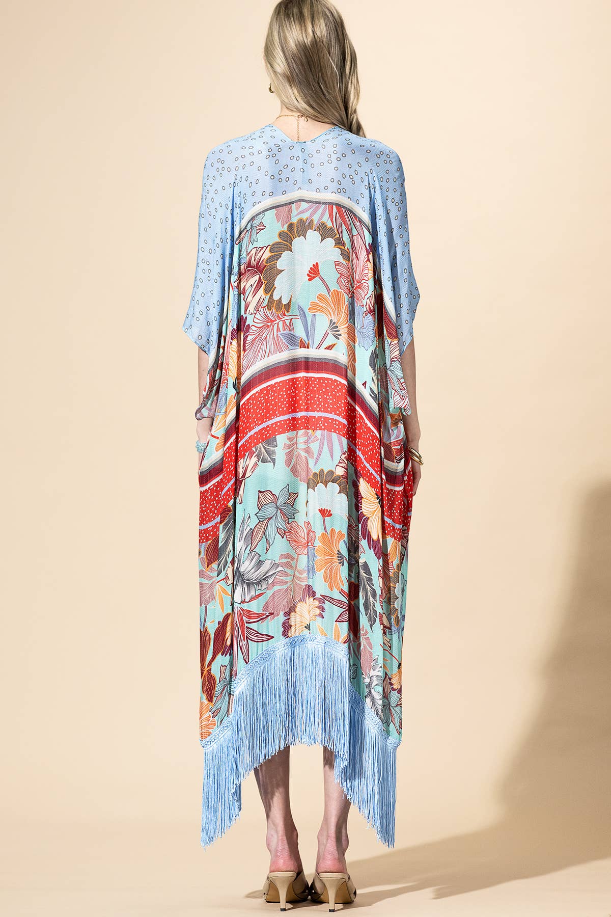 Woman wearing a colorful kimono-style garment with a floral pattern on a beige background
