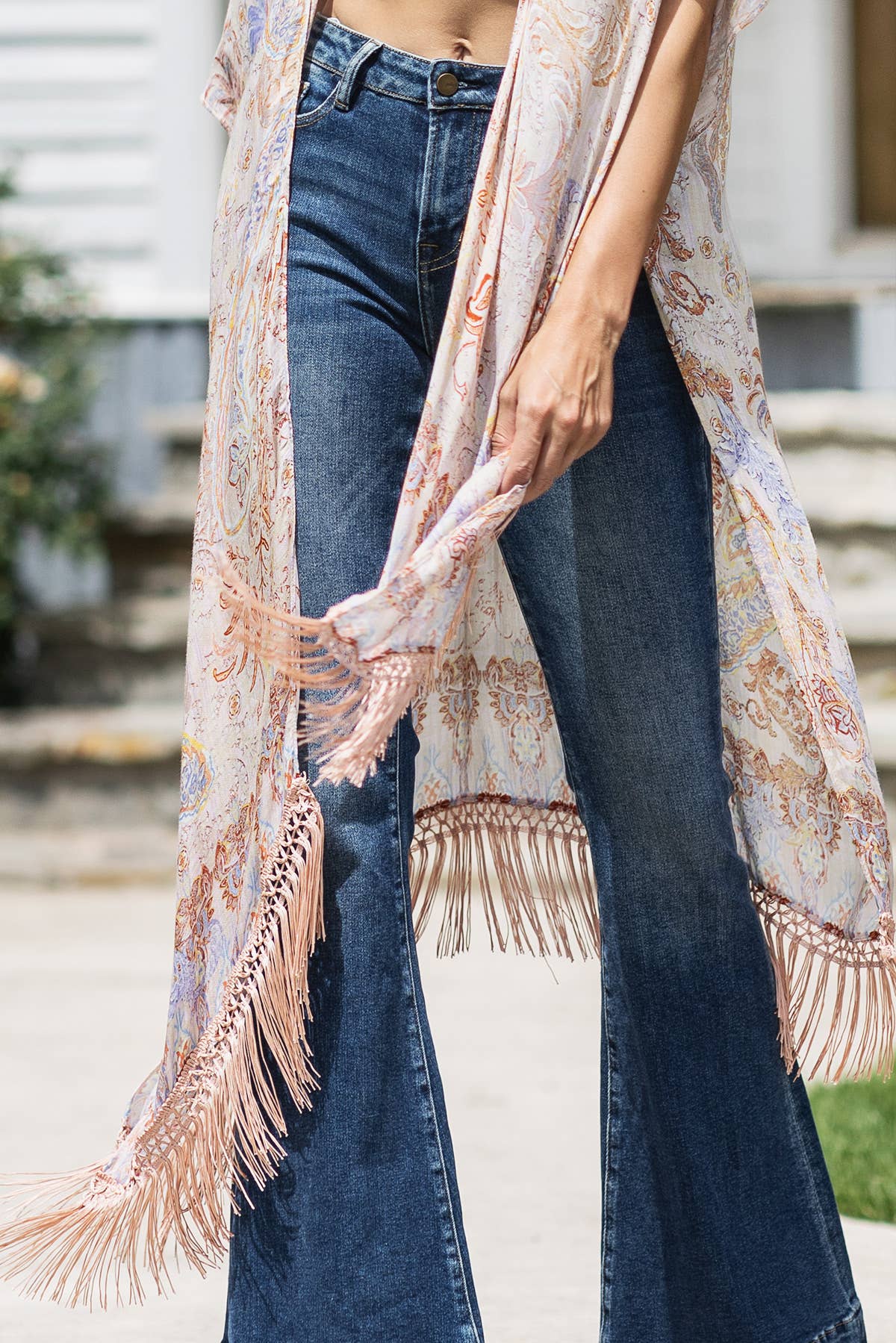 Person wearing a floral kimono with fringe details over jeans outdoors.