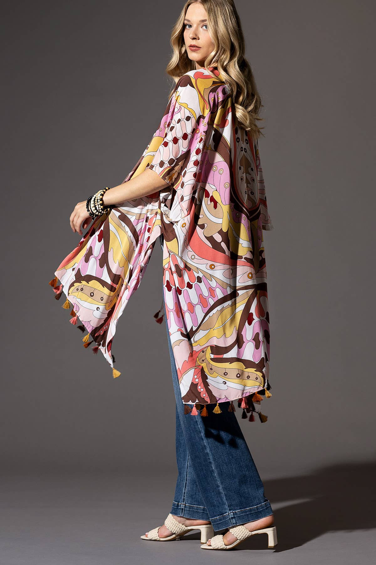 Woman wearing a colorful patterned scarf with tassels on a gray background