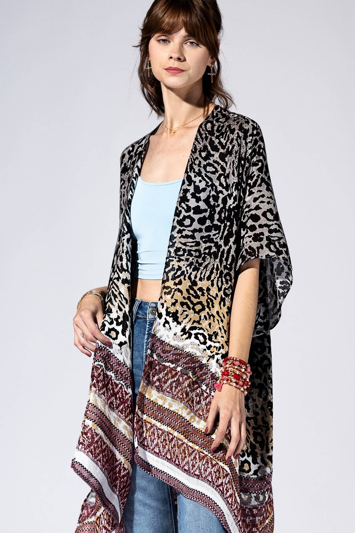 Woman wearing a leopard print kimono over a light blue top and jeans on a white background