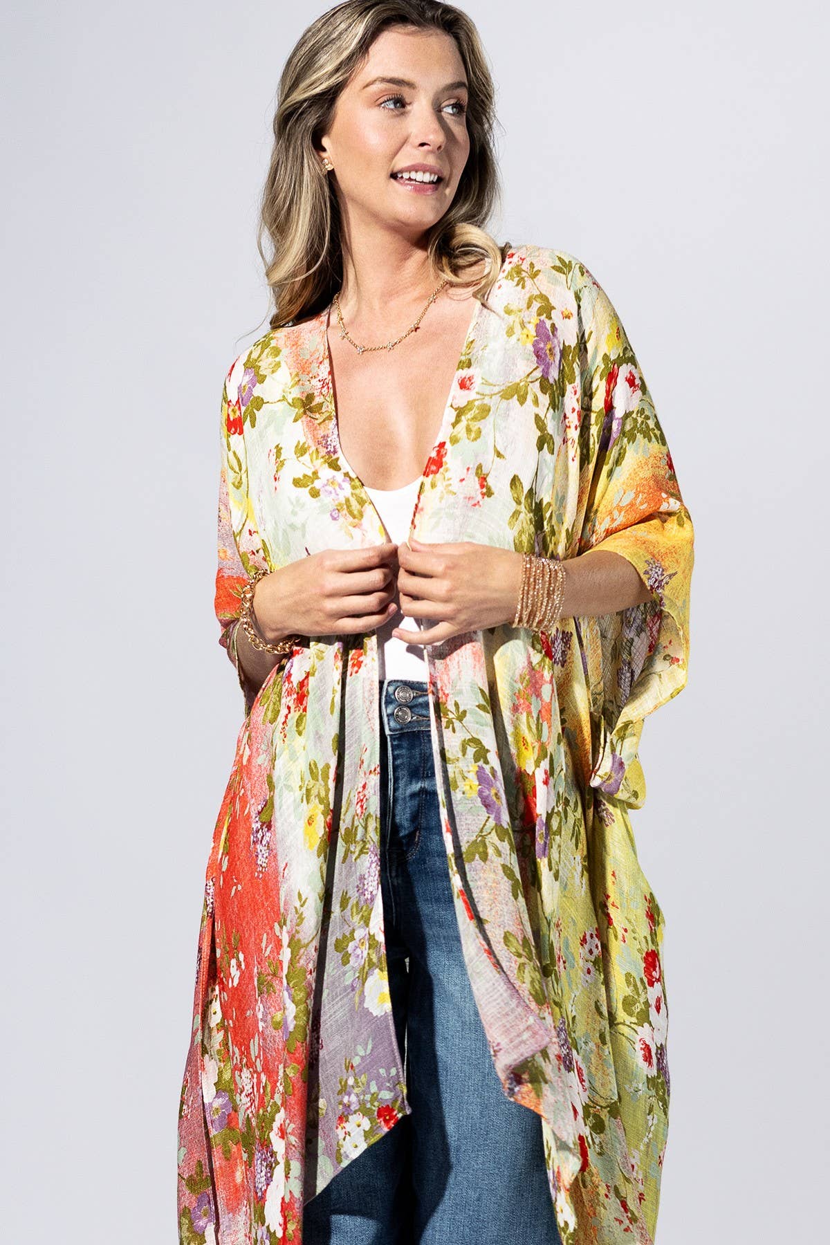 Woman wearing a colorful floral kimono over a white top and jeans on a light gray background