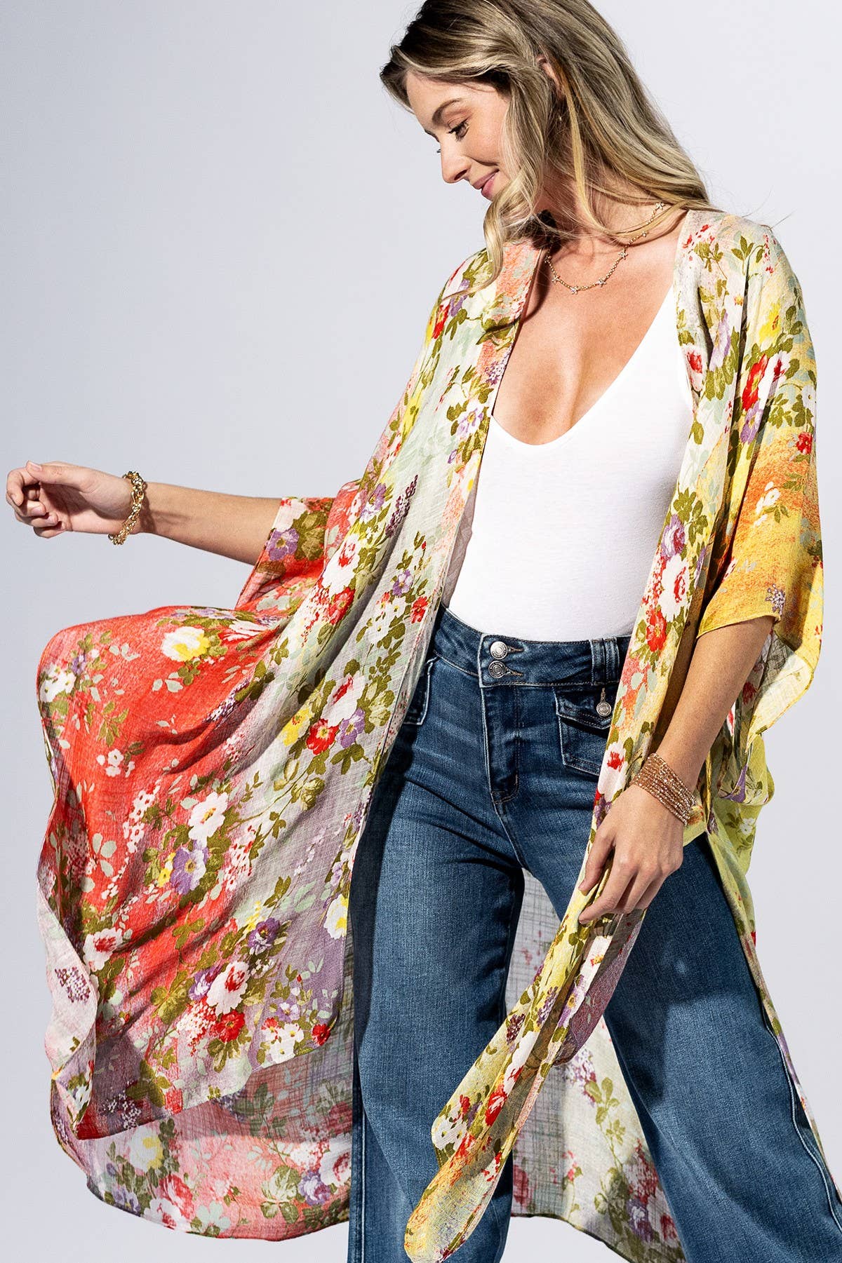 Woman wearing a floral kimono over a white top and blue jeans on a plain background